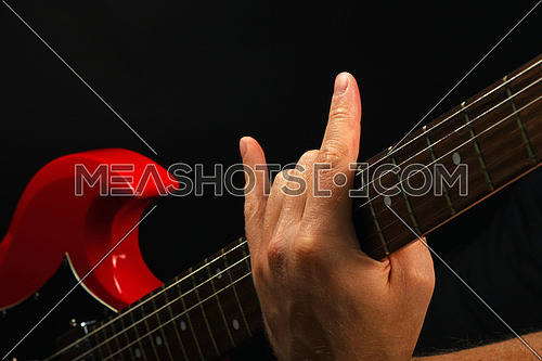 Male hand holding red sg guitar neck with devil horns rock metal sign isolated on black background