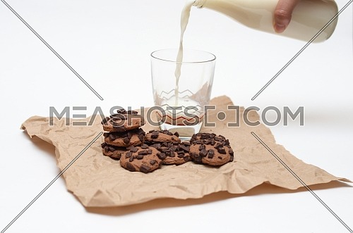 Milk poured from a glass bottle into a glass cup and chocolate chips cookies