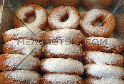 Close up many fresh ring donuts with sugar powder in retail display box, high angle view