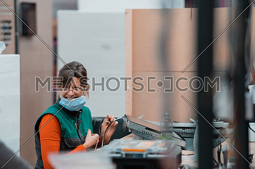 a woman sitting on a chair and assembles a screen for a machine, wearing a protective mask on her face due to a coronavirus pandemic. High quality photo