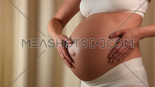 Close up profile view of pregnant Caucasian woman holding and touching her exposed belly with heart shaped hands anticipating baby birth
