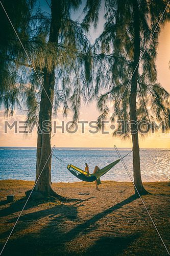 Silhouette of woman reading tablet in hammock,used split toning effect,vertical photo.