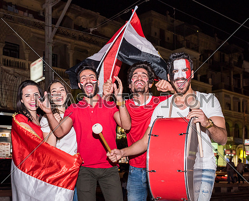 group of young people cheering for egypt, holding egyptian flags and drum while one of them has a paint egyptian flag on his face in the korba area at night