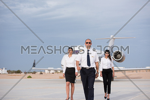 portrait of a successful middle eastern pilot with young beautiful stewardess at the airport in front of the private airplane