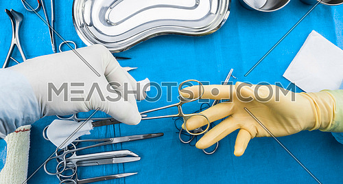 Surgeon working in operating room, hands with gloves holding scissors of suture and torundas, conceptual image, composicon horizontal