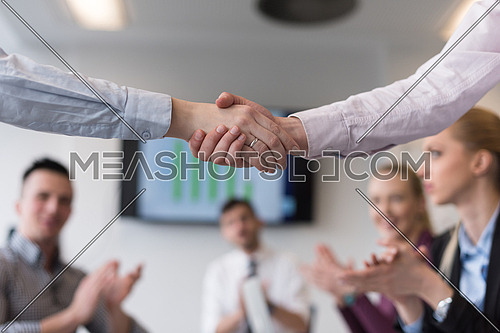 businesswomans handshake on team meeting  with group of people blured in background at modern startup business office interior