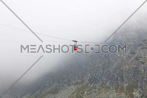 Red mountain cableway car lift in clouds and fog, low angle side view