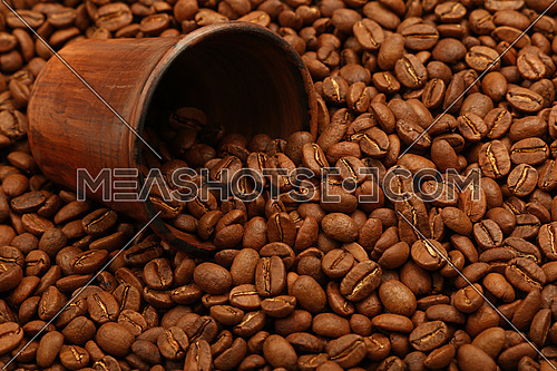 Close up fresh roasted Arabica coffee beans poured out of brown ceramic cup, high angle view