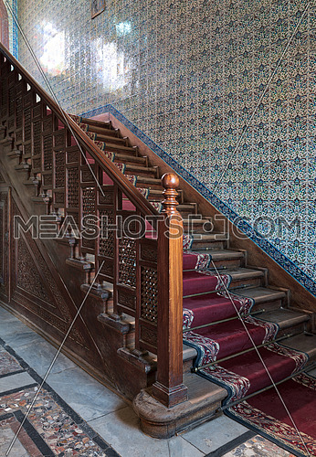 Wooden staircase with ornate red carpet, decorated wooden balustrade and Turkish ceramic tiles wall at the Residence hall, Manial Palace of Prince Mohammed Ali