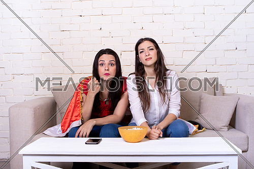 Two female friends watching TV and supporting Egyptian soccer team