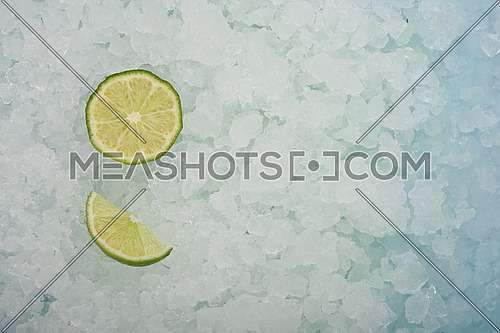 Close up fresh juicy green lime cut half and wedge slice over background of crushed ice, elevated high angle view, directly above