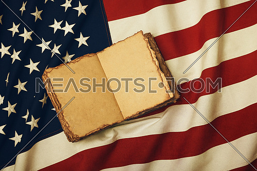 Close up vintage book blank yellow paper pages on old weathered cotton embroidered US national flag background, symbol of American history heritage, elevated high angle view, directly above