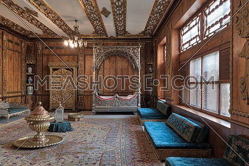 Cairo, Egypt - December 2, 2017: Manial Palace of Prince Mohammed Ali Tawfik. Residence of prince's mother with golden ornate niche, silver bed, golden wardrobe, blue couches, ornate wooden wall and ceiling