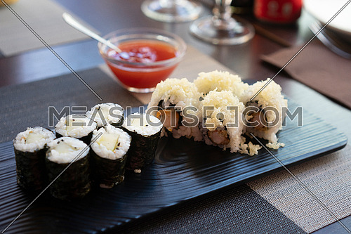 Traditional japanese rolls sushi with cucumbers and rolls sushi with shrimps fried on black plate at restaurant.Background sweet chili sauce.