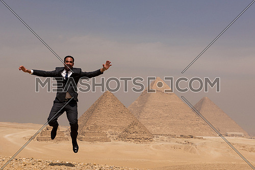 arabian business man jumping in desert with pyramids in background