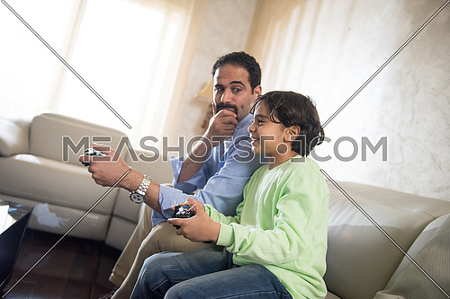 Middle Eastern father and son playing video games and cheerfully spend time on the sofa