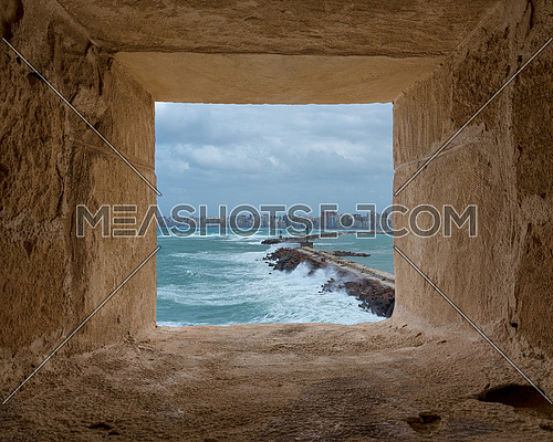 Stone window frame overlooking barrier and entrance of the old east harbor of Alexandria city at the Mediterranean Sea with skyline of the city at the far end, Egypt, includes clipping path for window