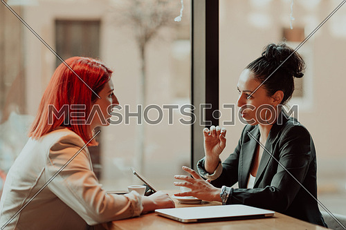 One-on-one meeting.Two young business women sitting at table in cafe.Girl using laptop, smartphone, blogging. Teamwork, business meeting. Freelancers working.