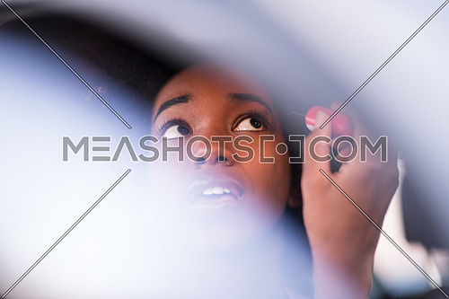 young beautiful African American woman enjoys while makeup herself in the car