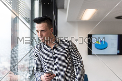 relaxed young businessman using smart phone at modern startup business office meeting room  with big window and city in backgronud