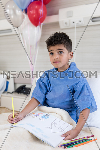 little middle eastern boyl painting home and family at hospita bed in a large modern hospital