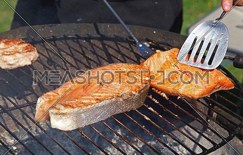 Close up cooking salmon fish steak and fillet on on bbq grill grate, high angle view