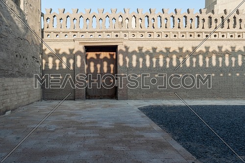 Stone bricks old decorated fence with wooden door and shadows of decorations of the opposite fence, Mosque of Ibn Tulun, Old Cairo, Egypt