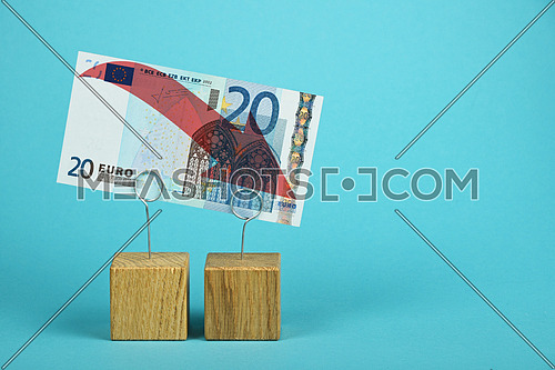 European economy crisis, decline of Euro currency, twenty Euro banknote with red arrow down at wooden metal holders over blue background