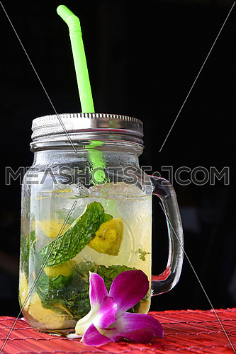 Big jars mug style full glass of fresh frozen mojito with metal cap lid, straw and purple orchid flower in cafe with black background