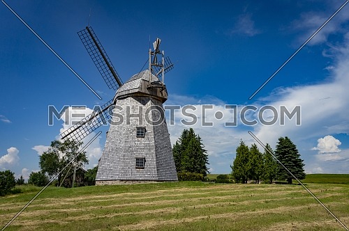 Old windmill in grassland in a country landscape with woodland trees under a cloudy blue sky in a scenic landscape