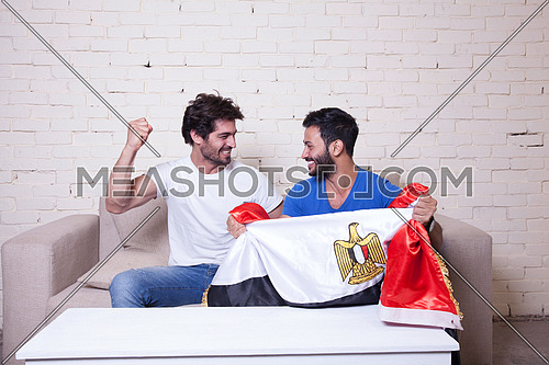 two young men sitting on a couch cheering for egypt