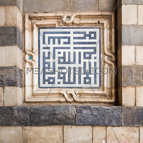 White and black marble decoration unit with Islamic calligraphy on the exterior stone wall of Sultan Hasan Mosque, Old Cairo, Egypt. Text translates: In The Name of Allah, the Beneficent, the Merciful