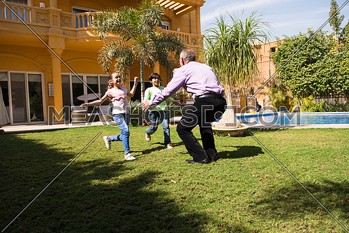 happy middle eastern grandfather enjoying with their grandchildren in the yard of a beautiful sunny day