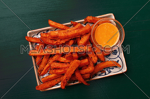 Portion of deep fried sweet potato chips or fries with dipping sauce on plate over table, elevated top view, directly above