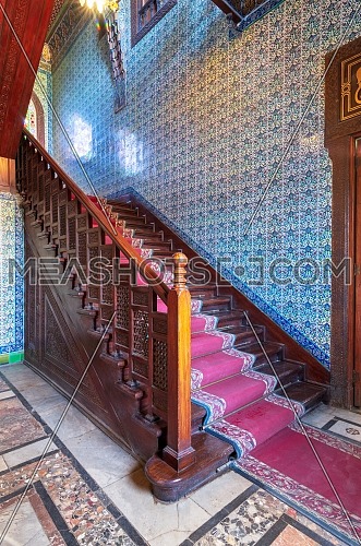 Wooden staircase with ornate red carpet, decorated wooden balustrade and Turkish ceramic tiles wall at the Residence hall, Manial Palace of Prince Mohammed Ali, Cairo, Egypt