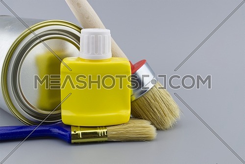 DIY, decorating or renovations concept with a still life with assorted clean paint brushes and unlabeled tin of paint over a grey background