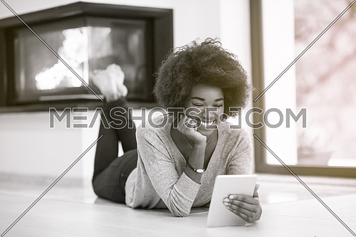 beautiful young black women used tablet computer on the floor of her luxury home in front of fireplace autumn day