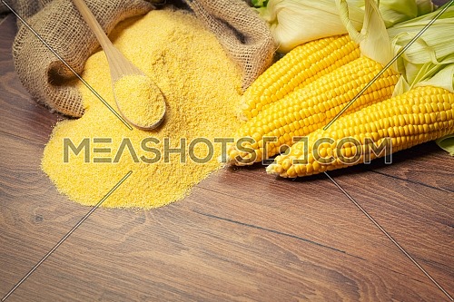 Ripe young sweet corn cob,on left stack cornmeal and spoon on top,wooden background, copy space.Gluten free food concept