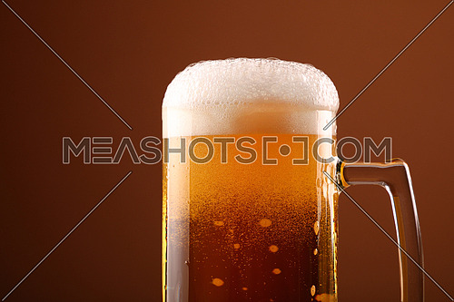 Close up pouring lager beer with white froth and bubbles in glass mug over dark brown background with copy space, low angle side view