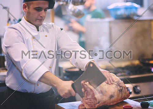 chef using ax while cutting big piece of beef  on wooden board in restaurant kitchen