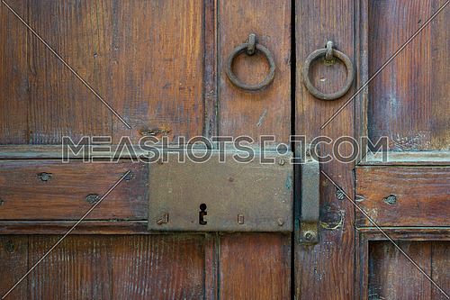 Closeup of a wooden aged latch and two rusted ring door knockers over an ornate wooden door, Cairo, Egypt