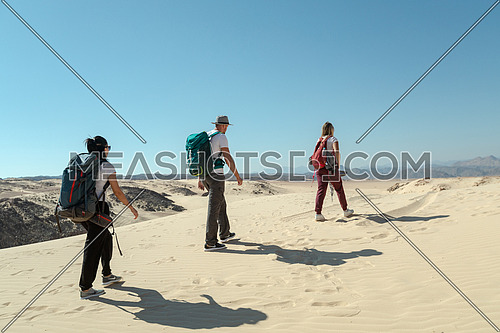 Long shot for group of tourists walking on sands with bedouin guide while exploring Sinai Trail from Ain Hodouda at day.