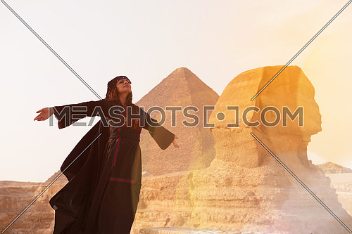 egyptian woman in traditional bedouin clothes in front of ancient great giza pyramids  and sphinx profile