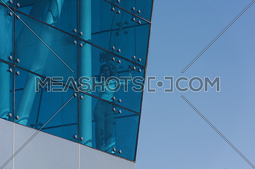 Outdoor shoot showing a female executive talking on the phone through the glass front of a corporate offices building with a background of blue sky