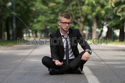 Young Businessman Sitting on Asphalt Begs For Money Outdoors In Park
