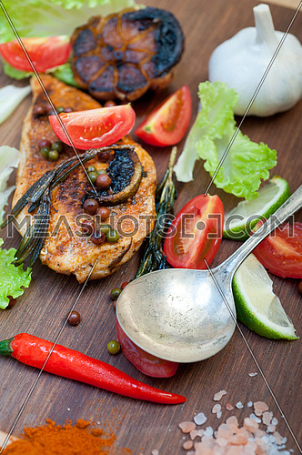wood fired hoven cooked chicken breast on wood board with herbs spices and vegetables