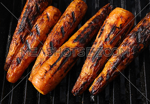 Close up cooking fresh new carrots in outdoor charcoal grill with cast iron metal grate, high angle view