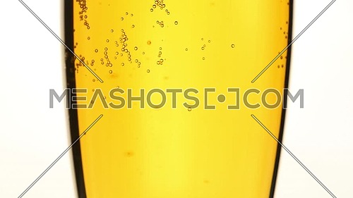 Close up background of pouring beer, sparkling wine or champagne with bubbles in glass, low angle side view, slow motion