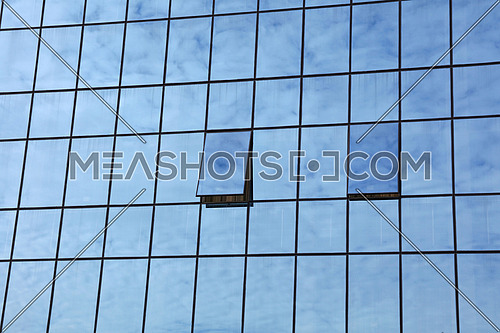 Cloudy blue sky reflection in glass of office business building with open windows, low angle view