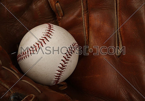 Close up one old baseball ball in worn vintage brown leather glove, high angle view